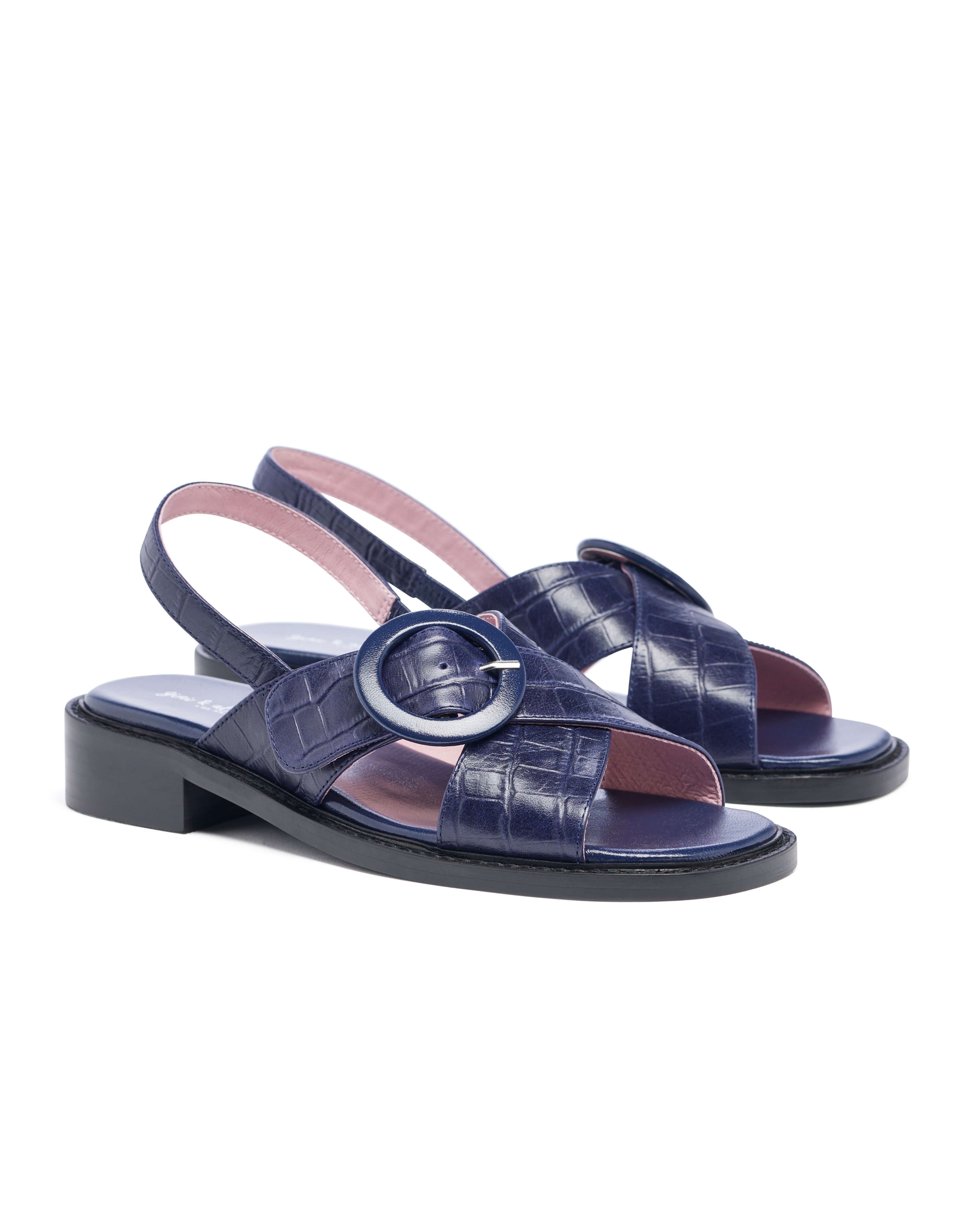 Navy blue sandals with a circular buckle on a white background