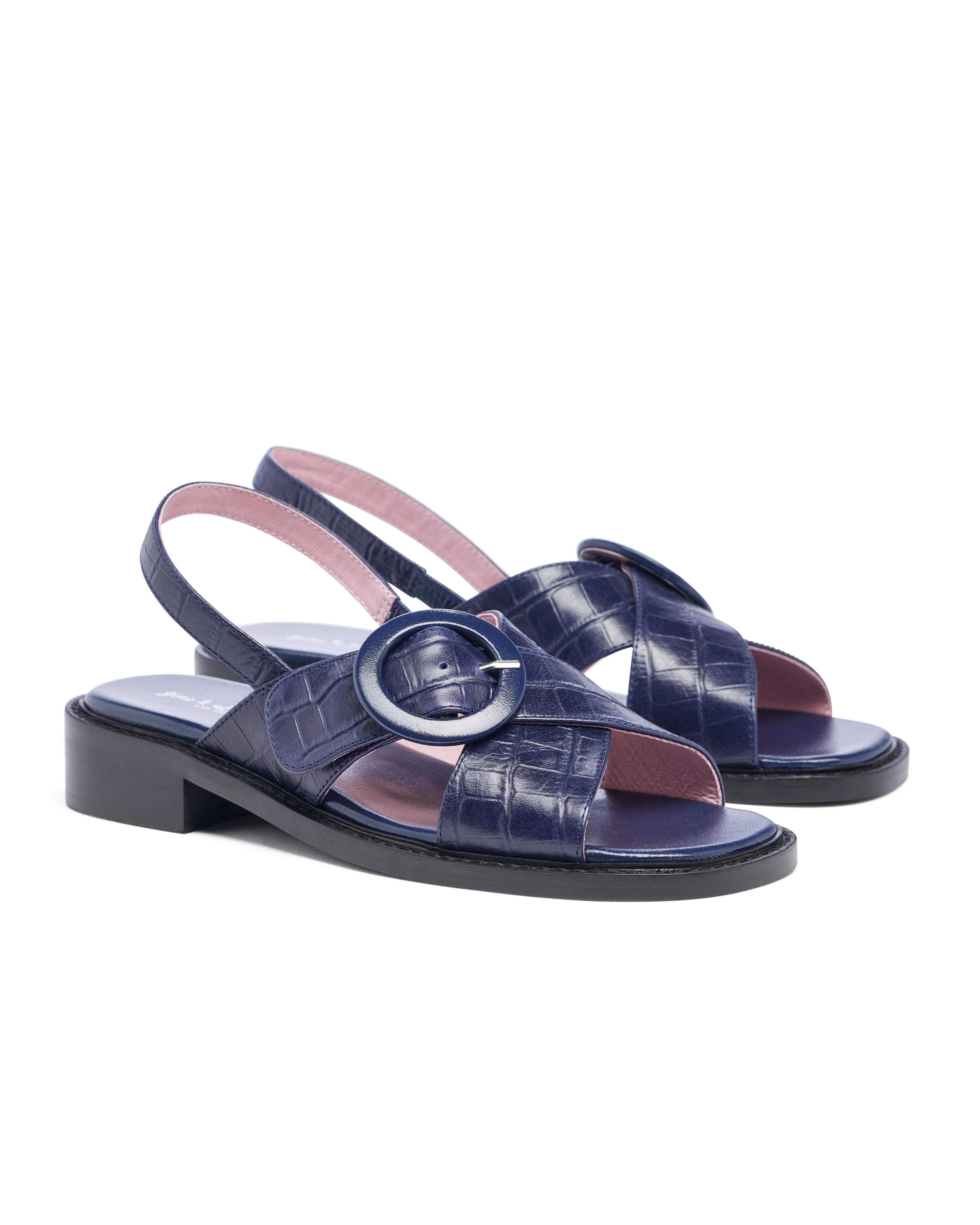 Navy blue sandals with a circular buckle on a white background